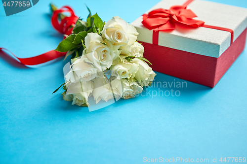 Image of Bouquet of white roses with red bow on blue background. Boxed gift on side