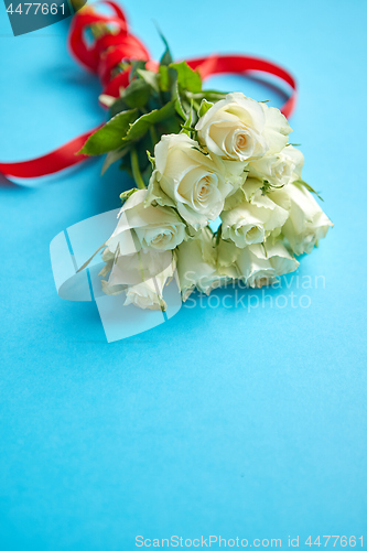 Image of Bouquet of white roses with red bow on blue background