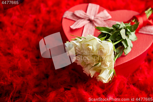 Image of Heart shaped boxed gift, placed on red feathers background