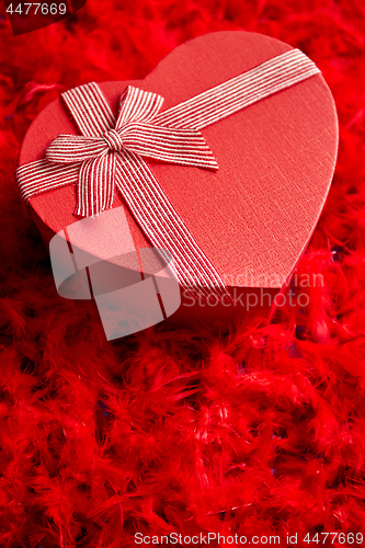 Image of Heart shaped boxed gift, placed on red feathers background