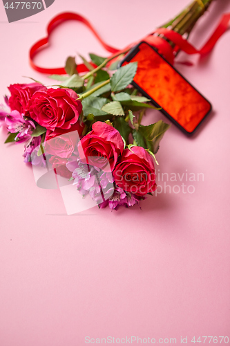 Image of Pink roses bouquet with hart shaped bow and mobile phone with copy space screen