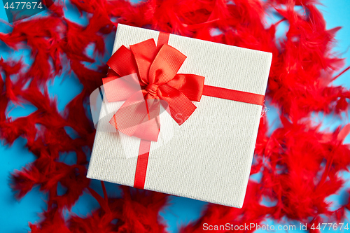 Image of Box with a gift, tied with a ribbon placed on red feathers