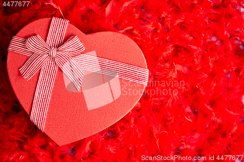 Image of Heart shaped boxed gift, placed on red feathers background