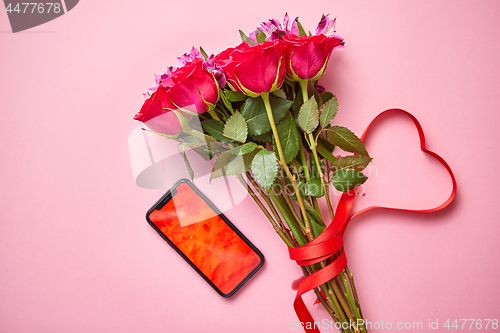 Image of Pink roses bouquet with hart shaped bow and mobile phone with copy space screen