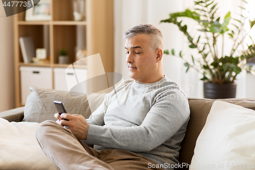 Image of man with smartphone sitting on sofa at home