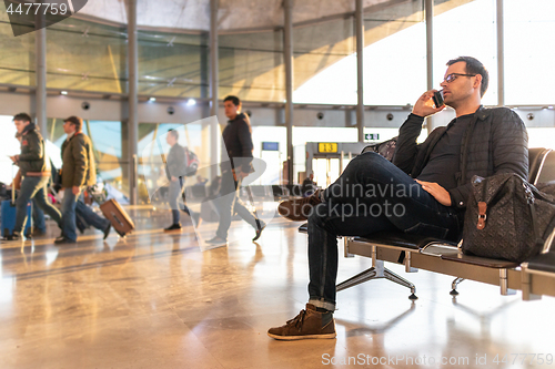 Image of Male traveler talking on his cell phone while waiting to board a plane at departure gates at airport terminal.