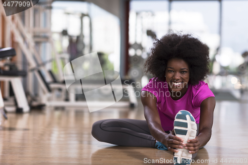 Image of woman in a gym stretching and warming up man in background worki