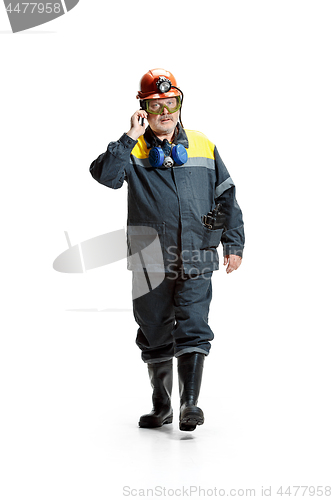 Image of The studio shot of serious senior bearded male miner in motion at the camera with smartphone on a white background.