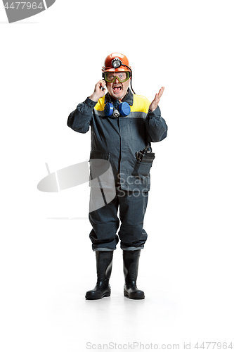 Image of The studio shot of angry senior bearded male miner standing at the camera with smartphone on a white background.