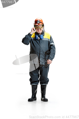 Image of The studio shot of angry senior bearded male miner standing at the camera with smartphone on a white background.