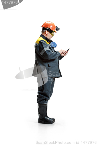 Image of The studio shot of serious senior bearded male miner standing at the camera with smartphone on a white background.