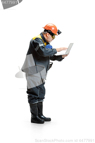 Image of The studio shot of pensive senior bearded male miner standing in profile view at the camera with laptop on a white background.