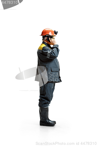 Image of The studio shot of serious senior bearded male miner standing in profile view at the camera with smartphone on a white background.