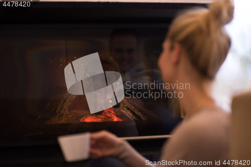 Image of young woman drinking coffee in front of fireplace