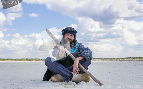 Image of Man In The Ethnic Clothes Shows A Sand By Hand Sitting In A Dese