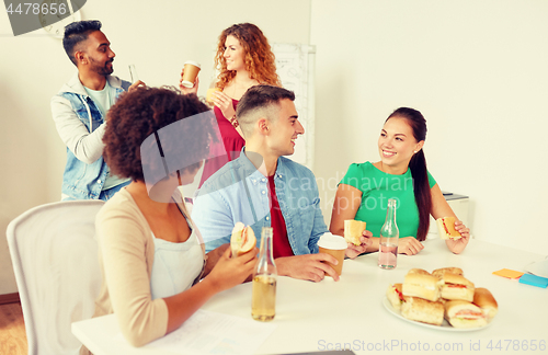 Image of happy friends or team eating at office