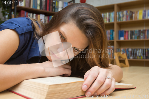 Image of Tired girl reading a book at the table in the library