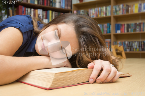 Image of The girl lay down on a book in the library and smiles having closed her eyes