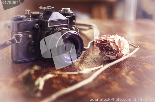 Image of Retro photo camera and dry rose on a wooden table