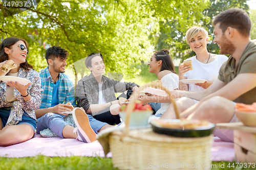Image of happy friends eating sandwiches at summer picnic