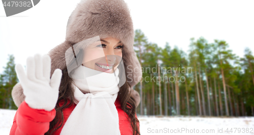 Image of happy woman in hat waving hand over winter forest