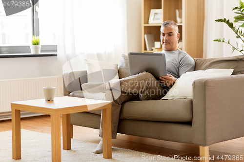 Image of man with laptop computer sitting on sofa at home