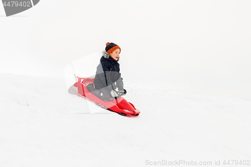 Image of happy boy sliding on sled down snow hill in winter