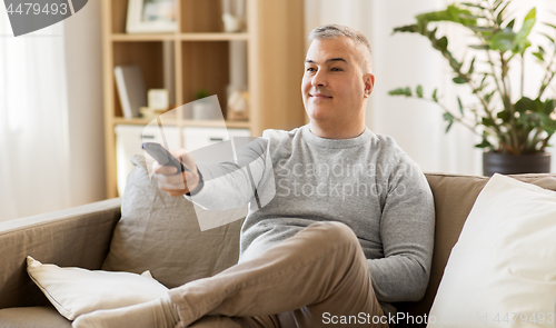 Image of man with remote control watching tv at home