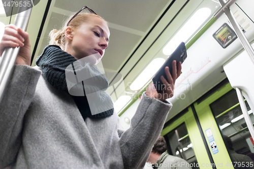 Image of Beautiful blonde woman wearing winter coat and scarf reading on the phone while traveling by metro public transport.