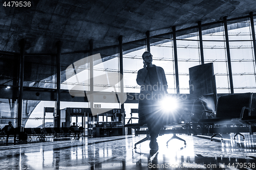 Image of Female traveler talking on her cell phone while waiting to board a plane at departure gates at airport terminal.