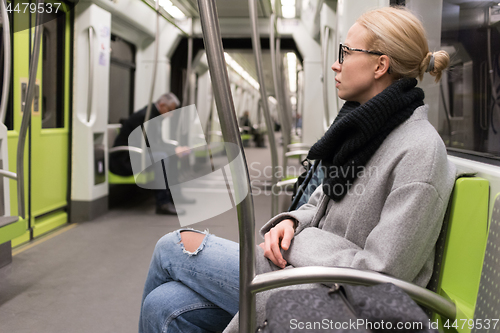 Image of Beautiful blond woman wearing winter coat and scarf traveling by metro. Public transport.