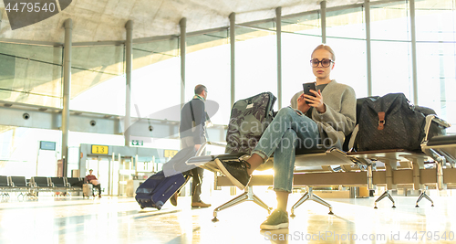 Image of Female traveler using her cell phone while waiting to board a plane at departure gates at airport terminal.