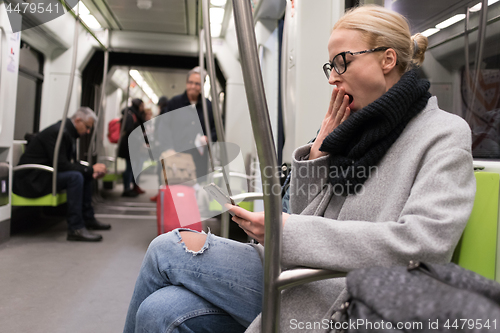 Image of Beautiful blond woman yawning while reading on the phone, traveling by metro. Public transport.