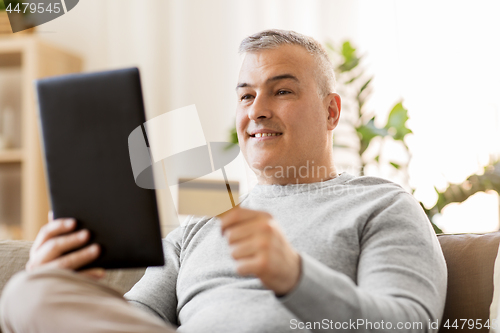 Image of man with tablet pc and credit card on sofa at home