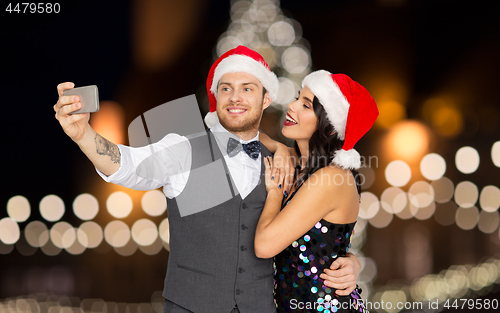 Image of couple in santa hats taking selfie at christmas