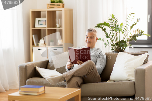 Image of man sitting on sofa and reading book at home