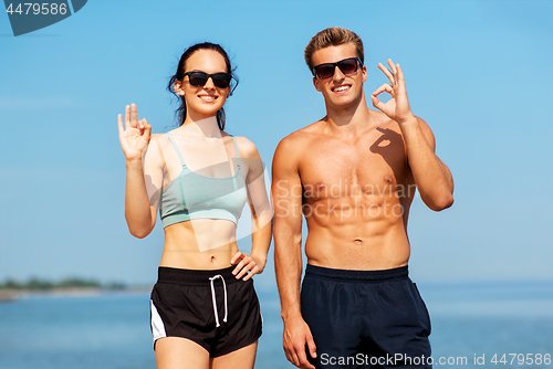 Image of couple of athletes in shades on beach showing ok