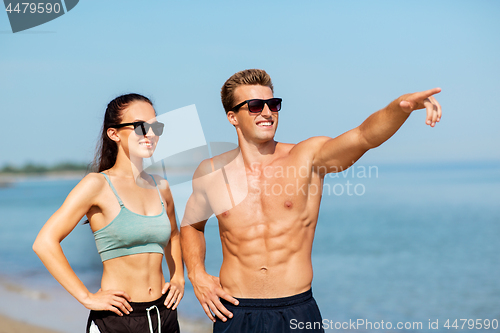 Image of happy couple in sports clothes and shades on beach