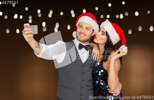 Image of couple in santa hats aking selfie at christmas