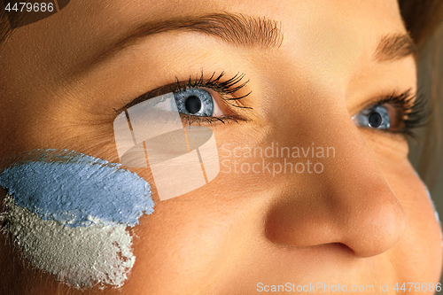 Image of Portrait of a woman with the flag of the Argentina painted on her face.