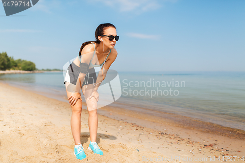 Image of female runner with earphones and arm band on beach