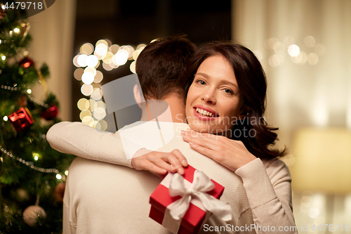 Image of happy couple with christmas gift hugging at home