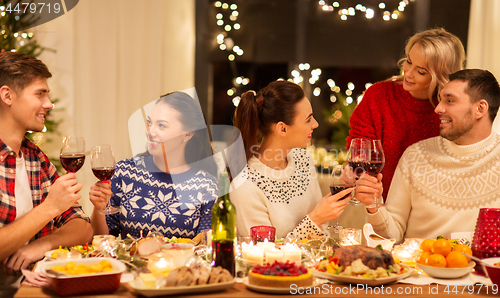 Image of happy friends drinking red wine at christmas party