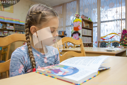 Image of A girl of ten years old is reading a book in the library