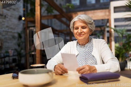 Image of senior woman with bill for coffee at street cafe