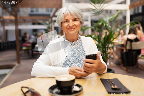 Image of happy senior woman with smartphone at street cafe