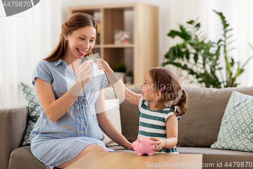 Image of pregnant mother and daughter with piggy bank