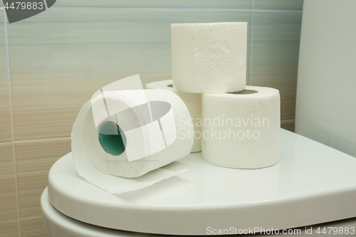 Image of Several rolls of toilet paper are on the toilet lid