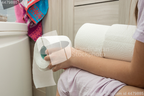 Image of The girl is sitting on the toilet and holding a few rolls of toilet paper