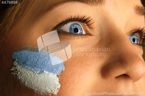 Image of Portrait of a woman with the flag of the Argentina painted on her face.